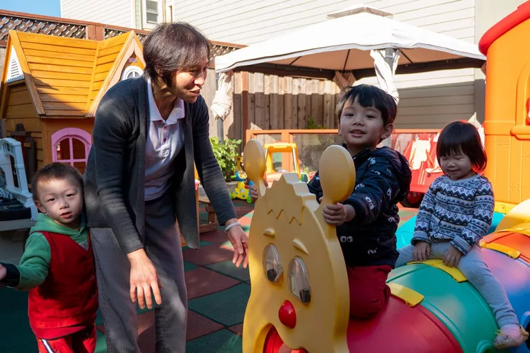 A teacher interacting with children in the outdoor playground